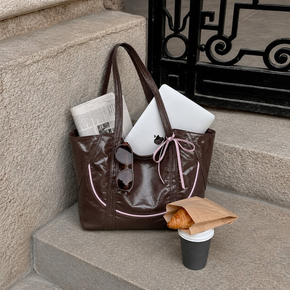 Clovara Glossy Tote Bag - Brown - packed with a laptop and newspaper on stone steps